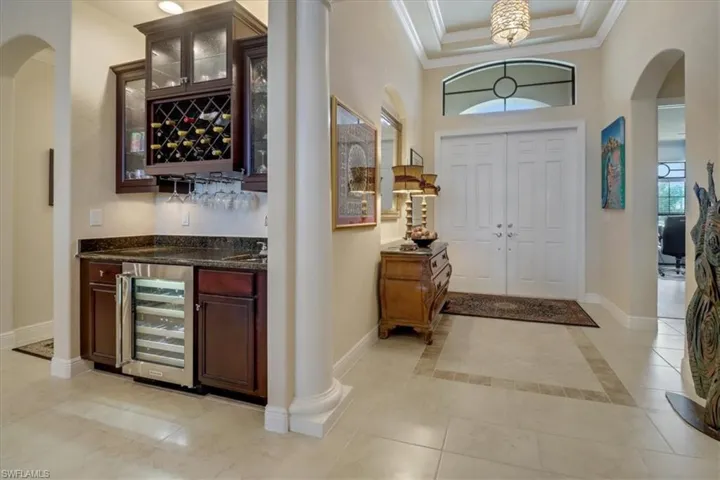 Tiled entrance foyer featuring ornate columns, a raised ceiling, wine cooler, and a healthy amount of sunlight