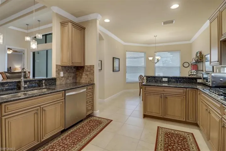 Kitchen featuring stainless steel dishwasher, sink, crown molding, light tile patterned flooring, and dark stone countertops