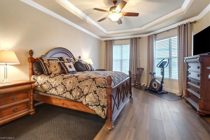 Bedroom featuring ceiling fan, crown molding, dark hardwood / wood-style flooring, and a tray ceiling
