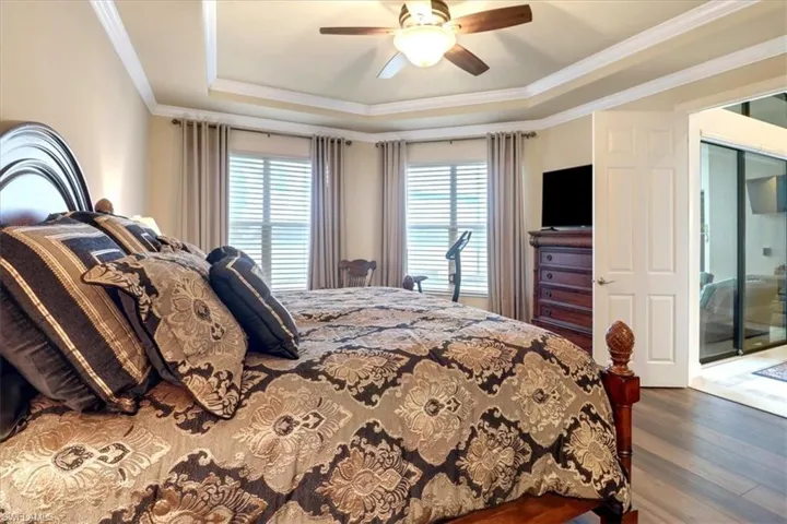 Bedroom with ceiling fan, wood-type flooring, ornamental molding, and a tray ceiling