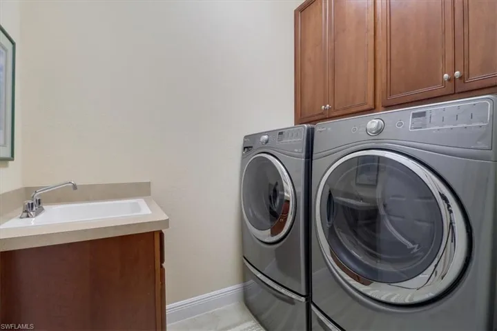 Clothes washing area featuring sink, washing machine and clothes dryer, and cabinets