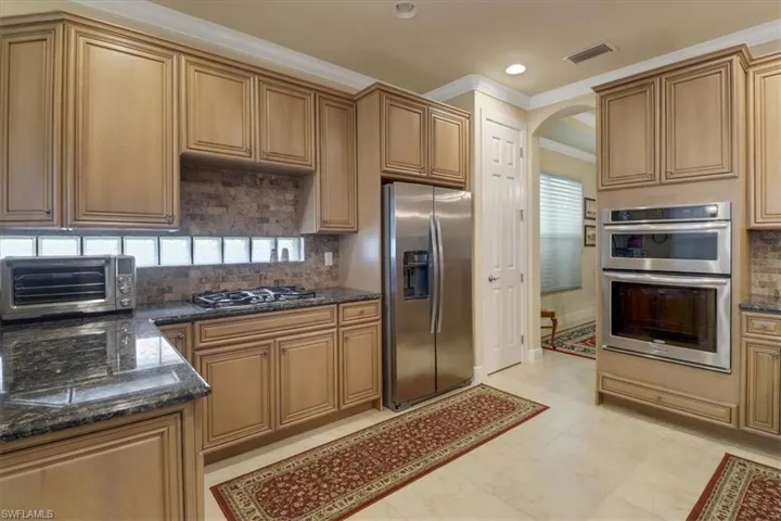 Kitchen featuring dark stone countertops, backsplash, light tile patterned floors, and stainless steel appliances