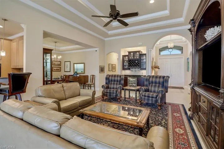 Tiled living room featuring a tray ceiling, crown molding, and ceiling fan with notable chandelier