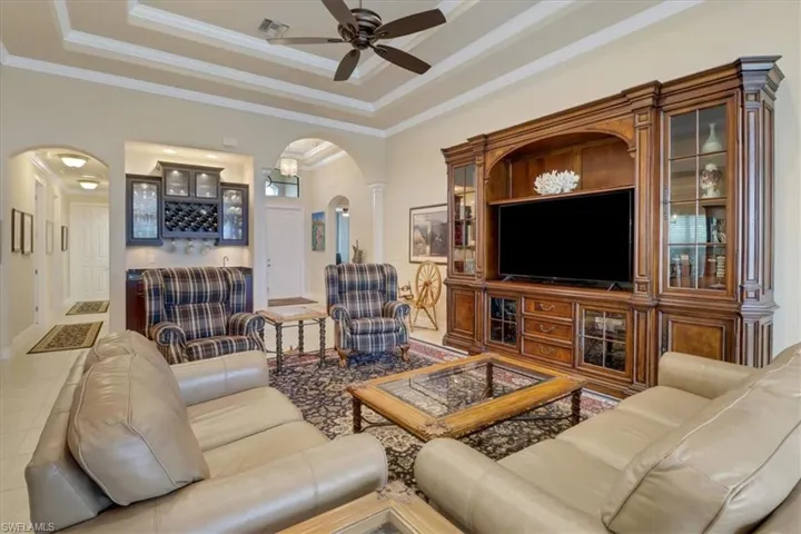Living room with ceiling fan, tile patterned flooring, a tray ceiling, and ornamental molding
