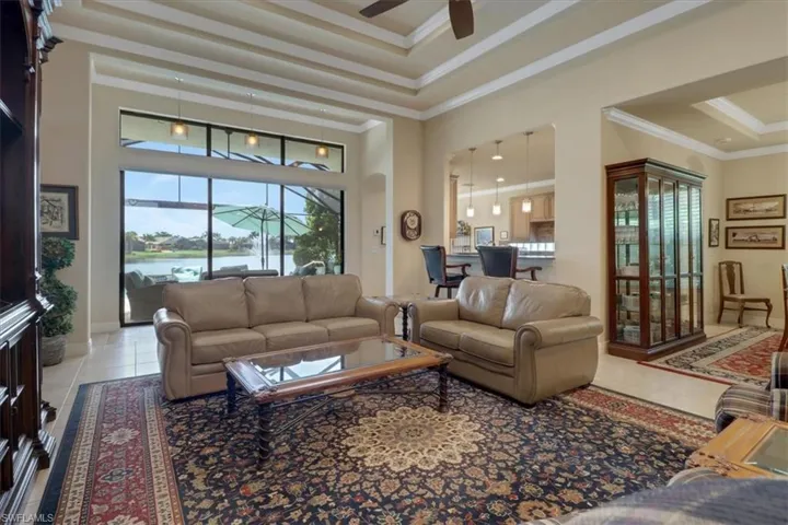 Tiled living room featuring ceiling fan, a tray ceiling, a high ceiling, crown molding, and a water view