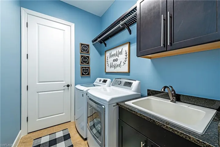 Laundry area featuring washer and clothes dryer, sink, light tile floors, and cabinets