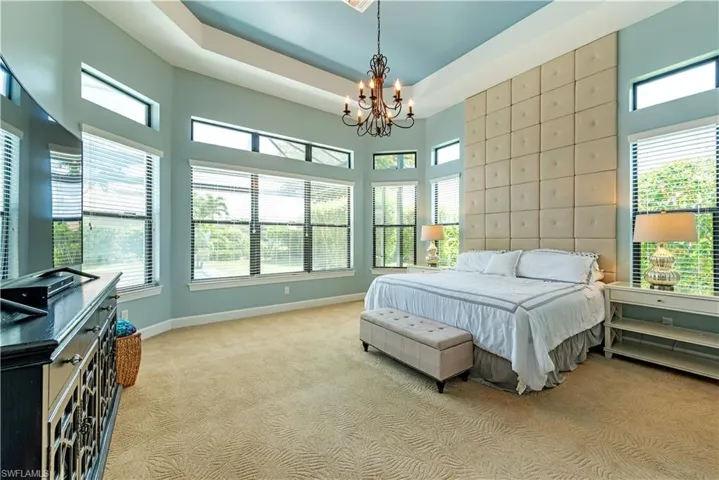 Bedroom featuring a raised ceiling, multiple windows, light carpet, and a chandelier
