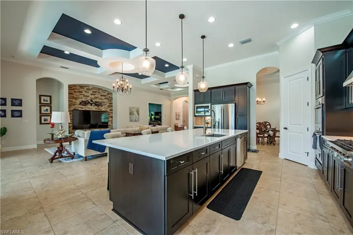 Kitchen featuring hanging light fixtures, ornamental molding, stainless steel appliances, an island with sink, and coffered ceiling