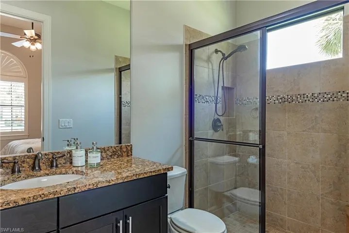 Bathroom with walk in shower, ceiling fan, vanity with extensive cabinet space, and toilet