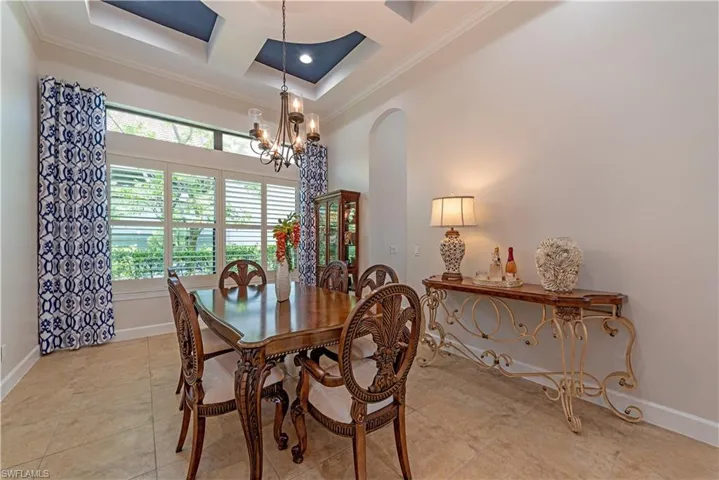 Tiled dining space with coffered ceiling, crown molding, and a notable chandelier