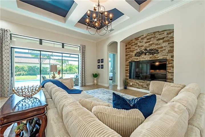 Tiled living room featuring coffered ceiling, ornamental molding, beamed ceiling, and a notable chandelier