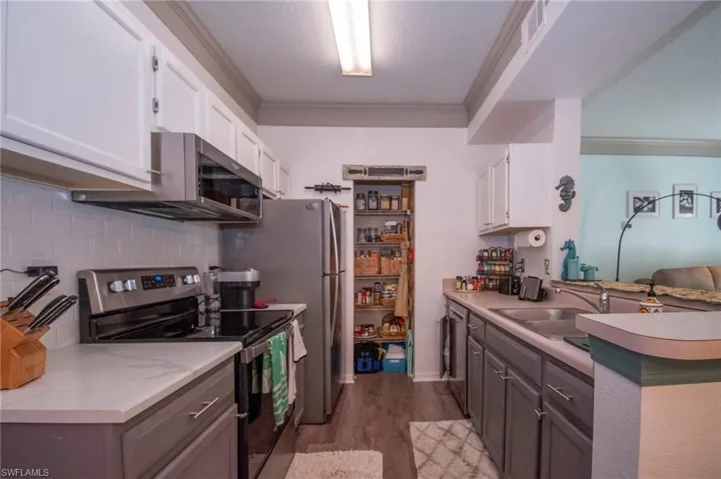 Kitchen featuring hardwood / wood-style floors, crown molding, stainless steel appliances, and white cabinets