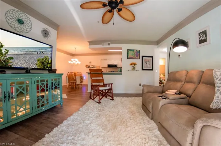 Living room with crown molding, ceiling fan with notable chandelier, and wood-type flooring