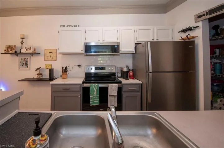 Kitchen with tasteful backsplash, white cabinetry, sink, crown molding, and stainless steel appliances
