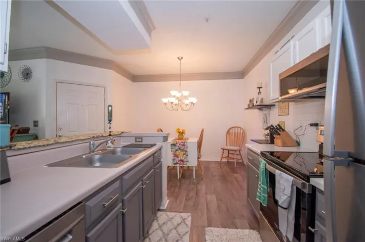 Kitchen with light hardwood / wood-style flooring, a chandelier, white cabinets, appliances with stainless steel finishes, and sink