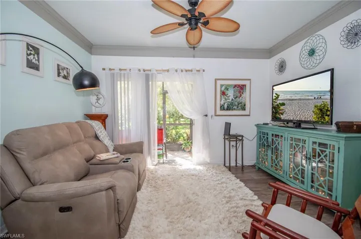 Living room with ceiling fan, crown molding, and dark wood-type flooring