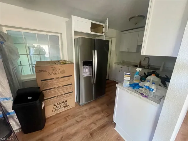 Kitchen featuring white cabinets, stainless steel refrigerator with ice dispenser, light wood-type flooring, and sink