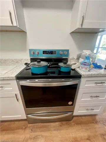 Room details featuring white cabinets, stainless steel electric range, light stone countertops, and light hardwood / wood-style flooring