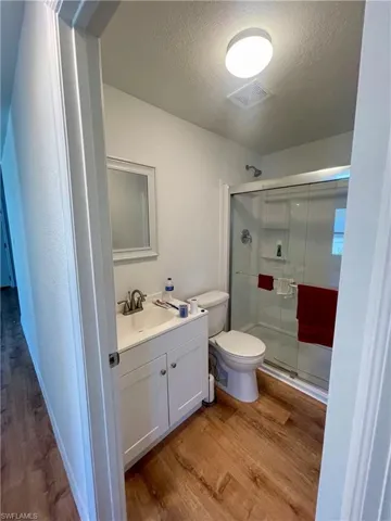 Bathroom with hardwood / wood-style flooring, toilet, walk in shower, and a textured ceiling