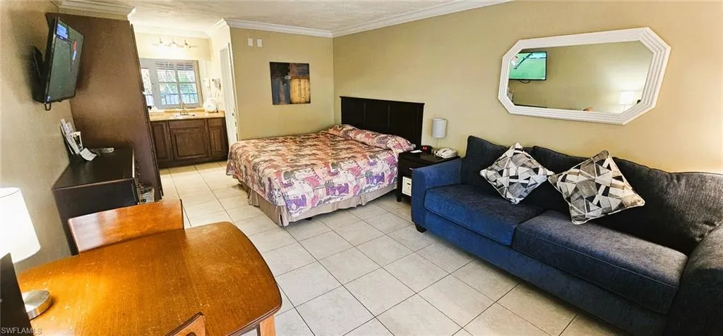 Bedroom with King Bed, Sofa, ensuite bath, light tile patterned floors, and crown molding