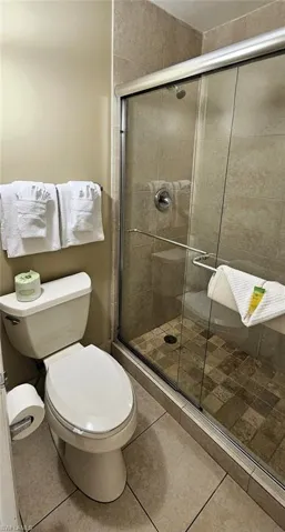 Bathroom with toilet, an enclosed shower, and tile patterned floors
