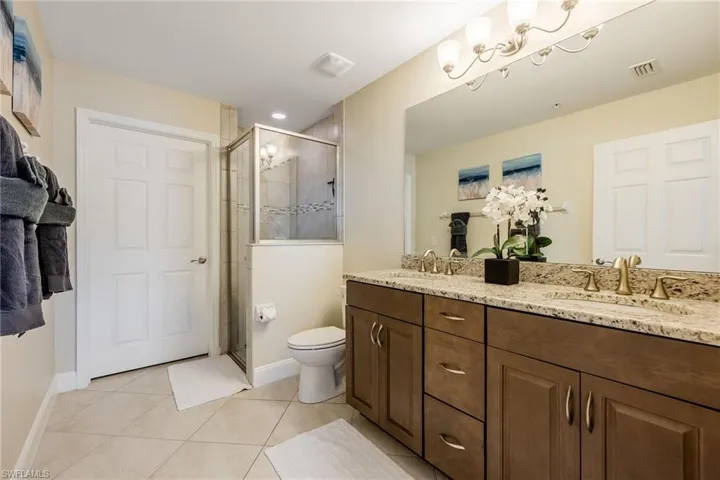 Bathroom with double vanity, light tile patterned flooring, and a shower stall