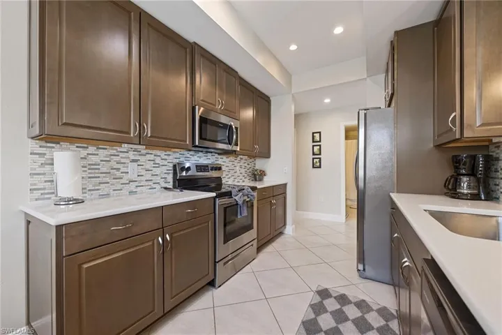 Kitchen with backsplash, appliances with stainless steel finishes, dark brown cabinets, light tile patterned floors, and recessed lighting
