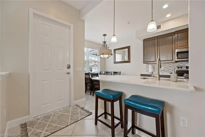 Kitchen featuring a breakfast bar area, light tile patterned flooring, decorative light fixtures, appliances with stainless steel finishes, and backsplash