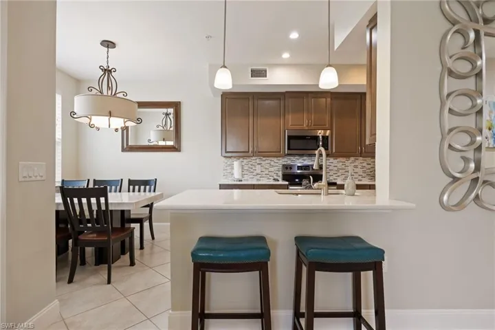 Kitchen with decorative light fixtures, decorative backsplash, a kitchen breakfast bar, appliances with stainless steel finishes, and light stone counters