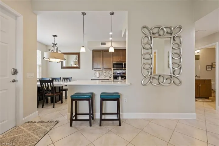Kitchen featuring brown cabinets, pendant lighting, a breakfast bar, tasteful backsplash, and light tile patterned floors