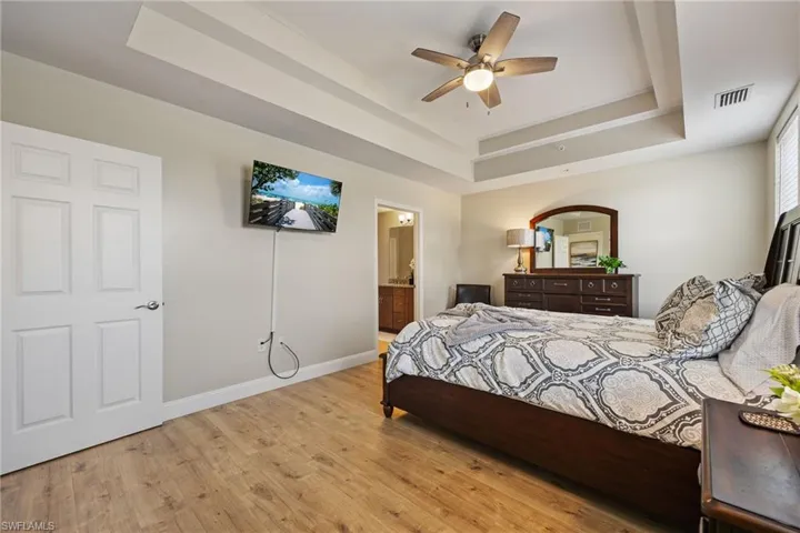Bedroom featuring a tray ceiling, light wood-style floors, ceiling fan, and ensuite bathroom