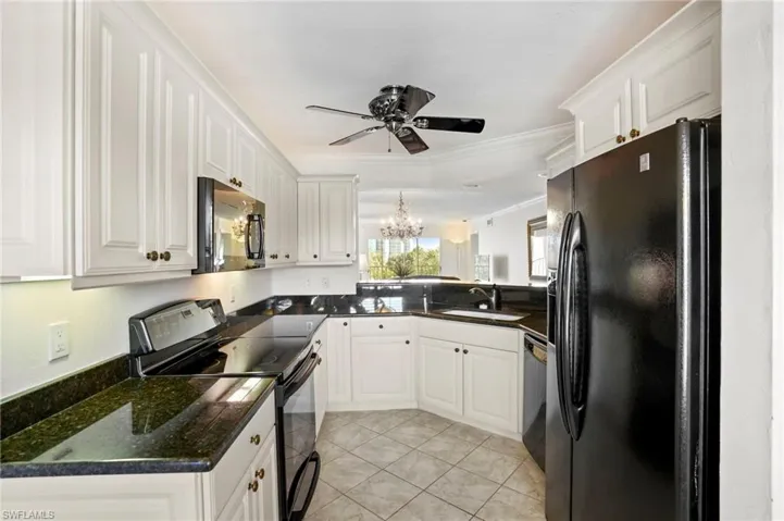 Kitchen with black appliances, a chandelier, white cabinetry, ornamental molding, and dark stone countertops