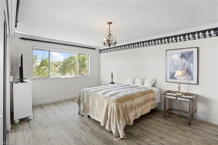 Bedroom with hanging lights, light wood-style flooring, and crown molding