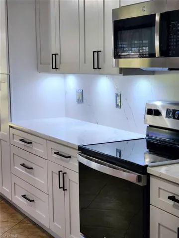 Kitchen with light tile patterned floors, appliances with stainless steel finishes, light stone counters, white cabinetry, and decorative backsplash