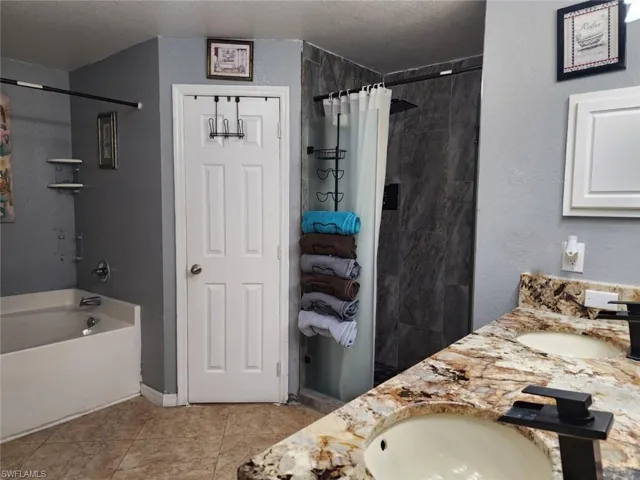 Bathroom with vanity, a textured ceiling, shower / bath combination with curtain, and tile patterned flooring