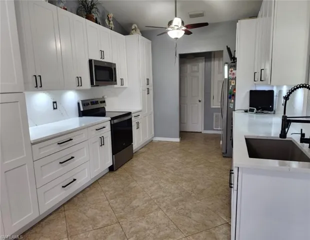 Kitchen featuring stainless steel appliances, sink, ceiling fan, decorative backsplash, and white cabinets