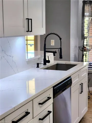Renovated Kitchen featuring dishwasher, white cabinetry, plenty of natural light, and light stone countertops