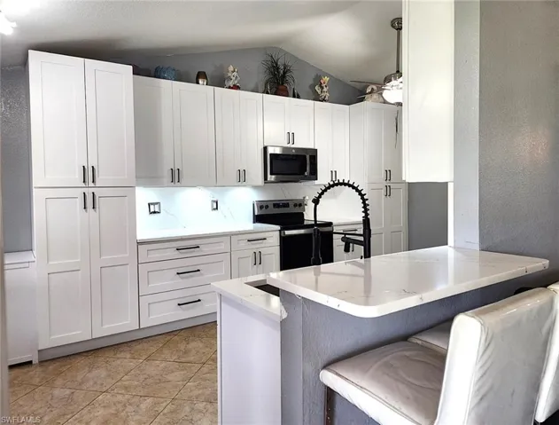 Kitchen with vaulted ceiling, appliances with stainless steel finishes, white cabinetry, kitchen peninsula, and a breakfast bar area