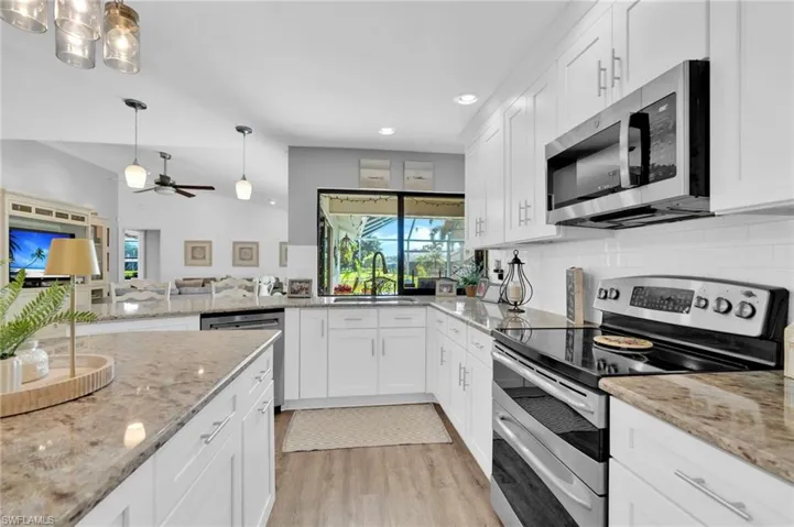 Kitchen featuring stainless steel appliances, white cabinets, pendant lighting, light stone countertops, and recessed lighting
