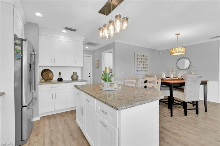 Kitchen featuring stainless steel refrigerator with ice dispenser, pendant lighting, white cabinetry, light stone counters, and light wood-style flooring