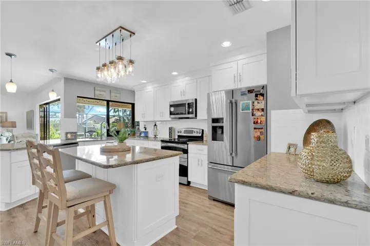 Kitchen featuring a breakfast bar, appliances with stainless steel finishes, white cabinetry, light stone countertops, and decorative backsplash