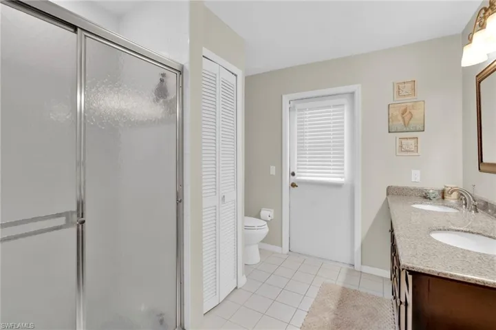 Bathroom featuring a closet, double vanity, light tile patterned floors, and a stall shower