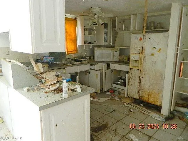 Kitchen with white microwave, ceiling fan, a peninsula, and white cabinetry