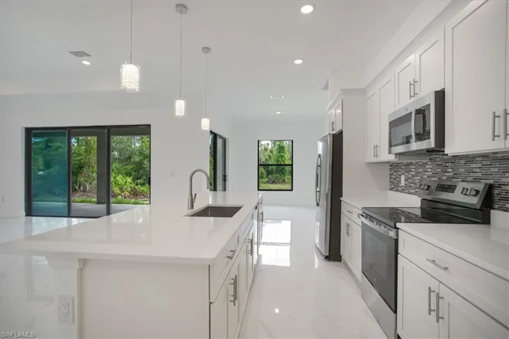 Kitchen featuring white cabinetry, stainless steel appliances, an island with sink, sink, and light tile floors