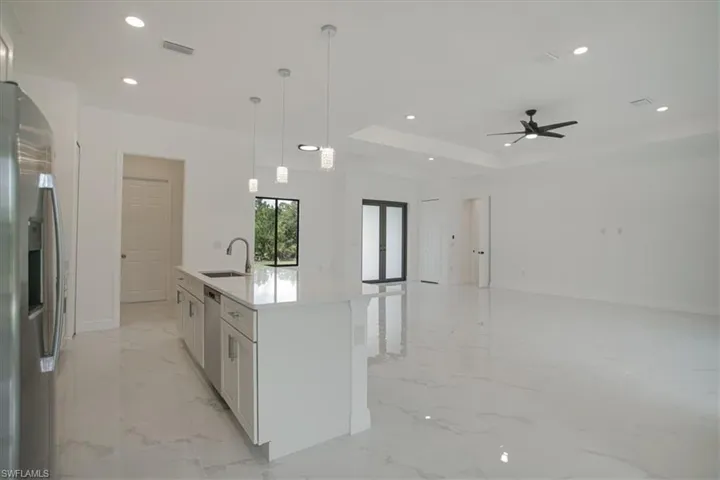 Kitchen with white cabinetry, stainless steel appliances, an island with sink, light tile flooring, and a raised ceiling