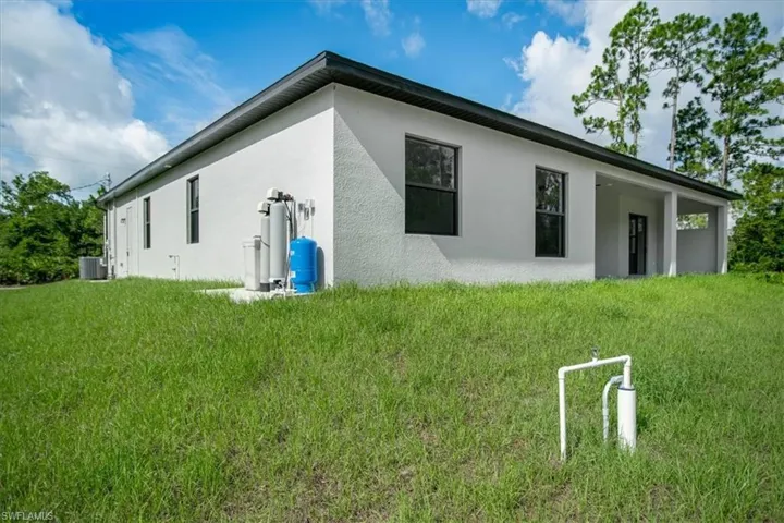 Rear view of house with central air condition unit and a lawn