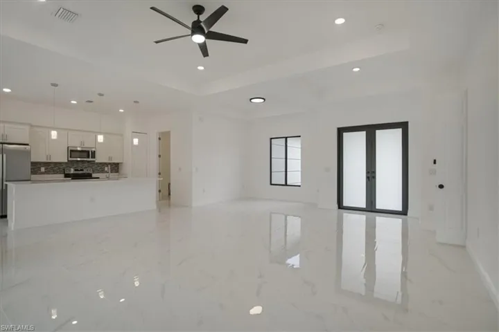 Unfurnished living room featuring french doors, sink, ceiling fan, light tile floors, and a raised ceiling