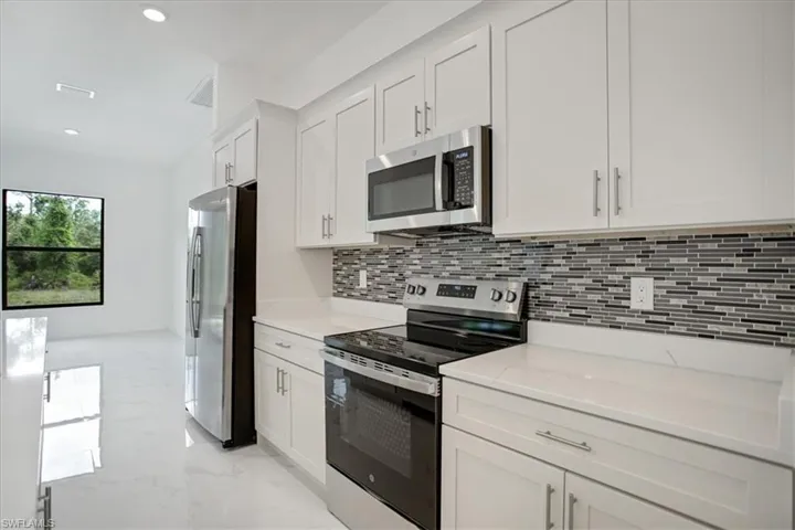 Kitchen featuring light stone counters, light tile flooring, stainless steel appliances, backsplash, and white cabinets