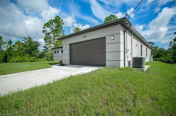 View of property exterior with a garage, central AC unit, and a lawn
