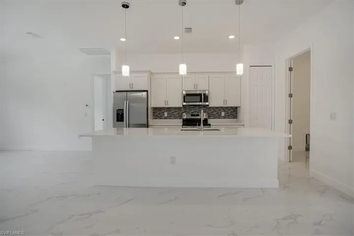 Kitchen with stainless steel appliances, a kitchen island with sink, backsplash, pendant lighting, and light tile floors